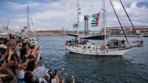 A ship of the Global Sumud Flotilla departing from harbour, as supporters on the dock cheer on and greet it.